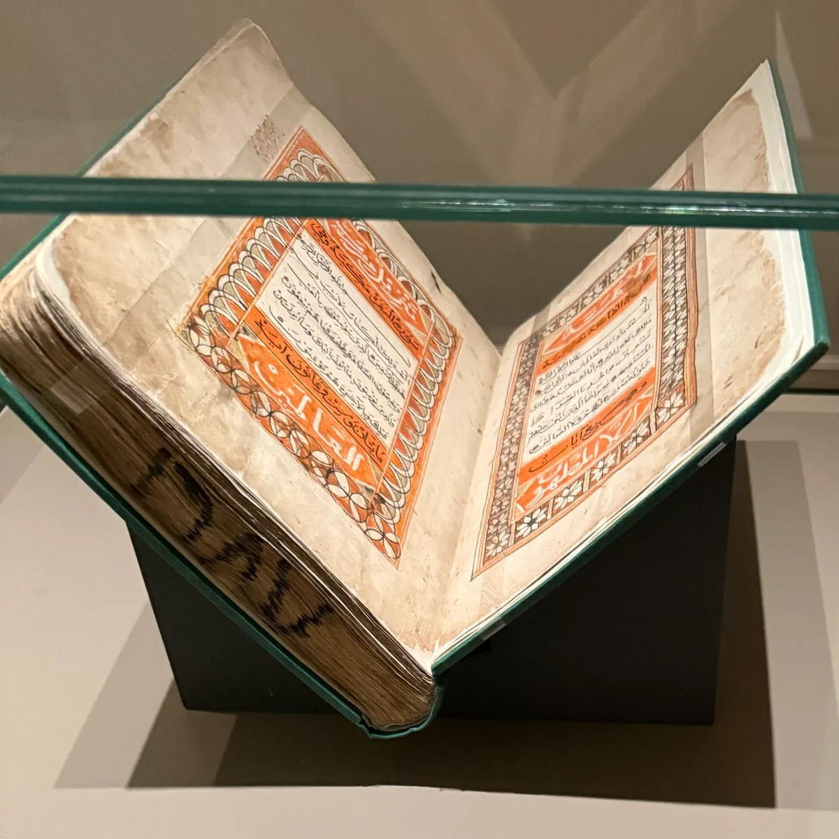 An illuminated Qur'an manuscript open on a stand in a museum display case