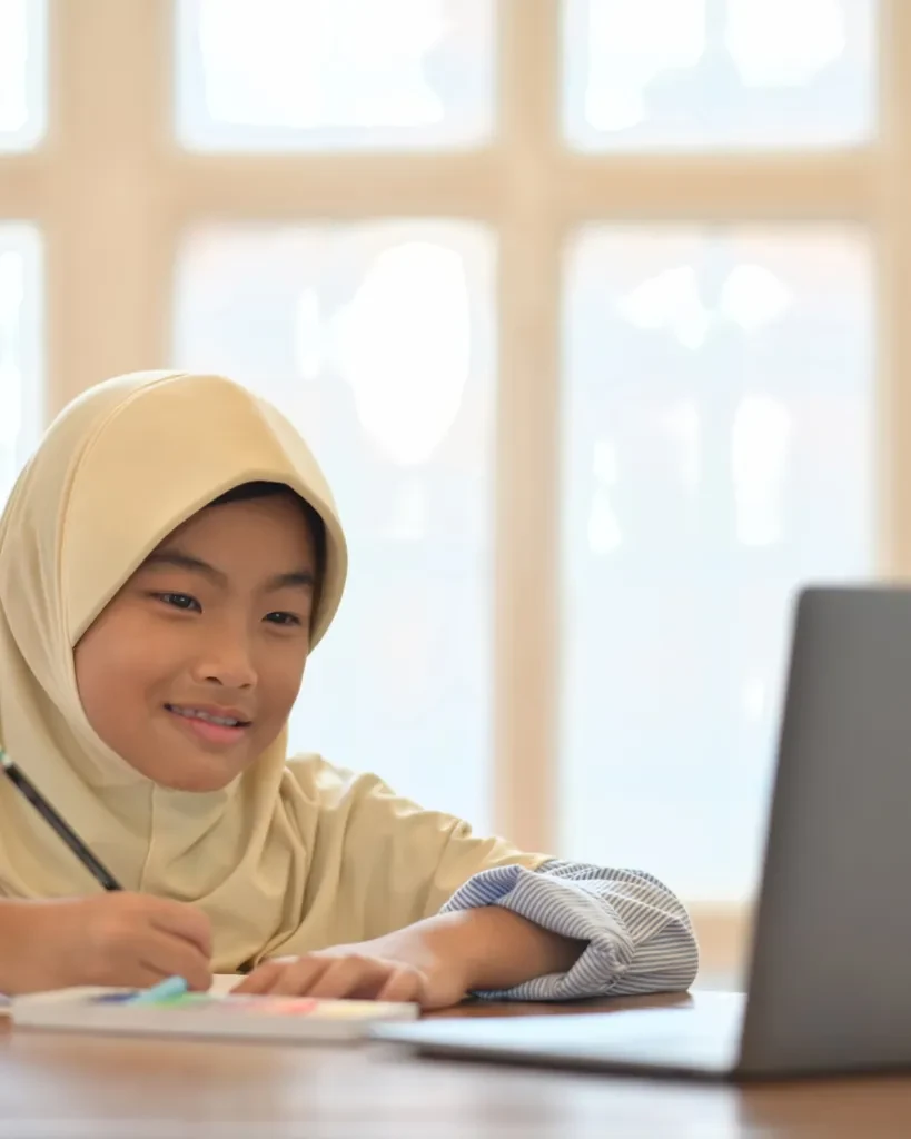 A young student smiling as she works at a laptop