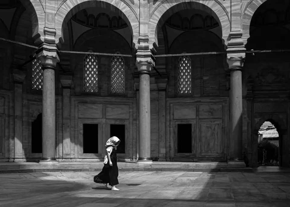 A woman in a headscarf walking across a mosque courtyard beneath stone arches