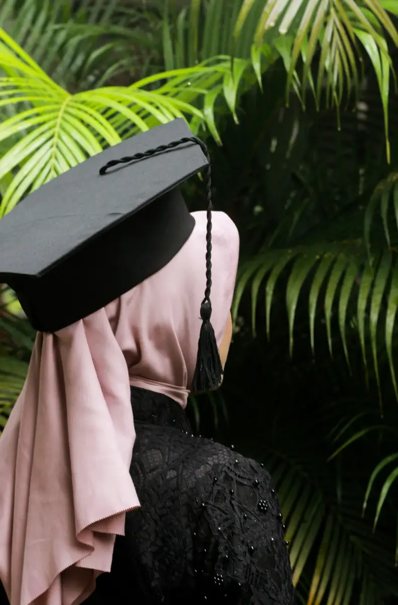 A young woman in a pink hijab and a graduation cap, seen from behind